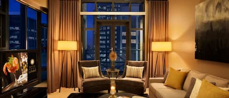 A modern hotel room with a large window, two armchairs, a sofa, a coffee table, and a flat-screen TV.