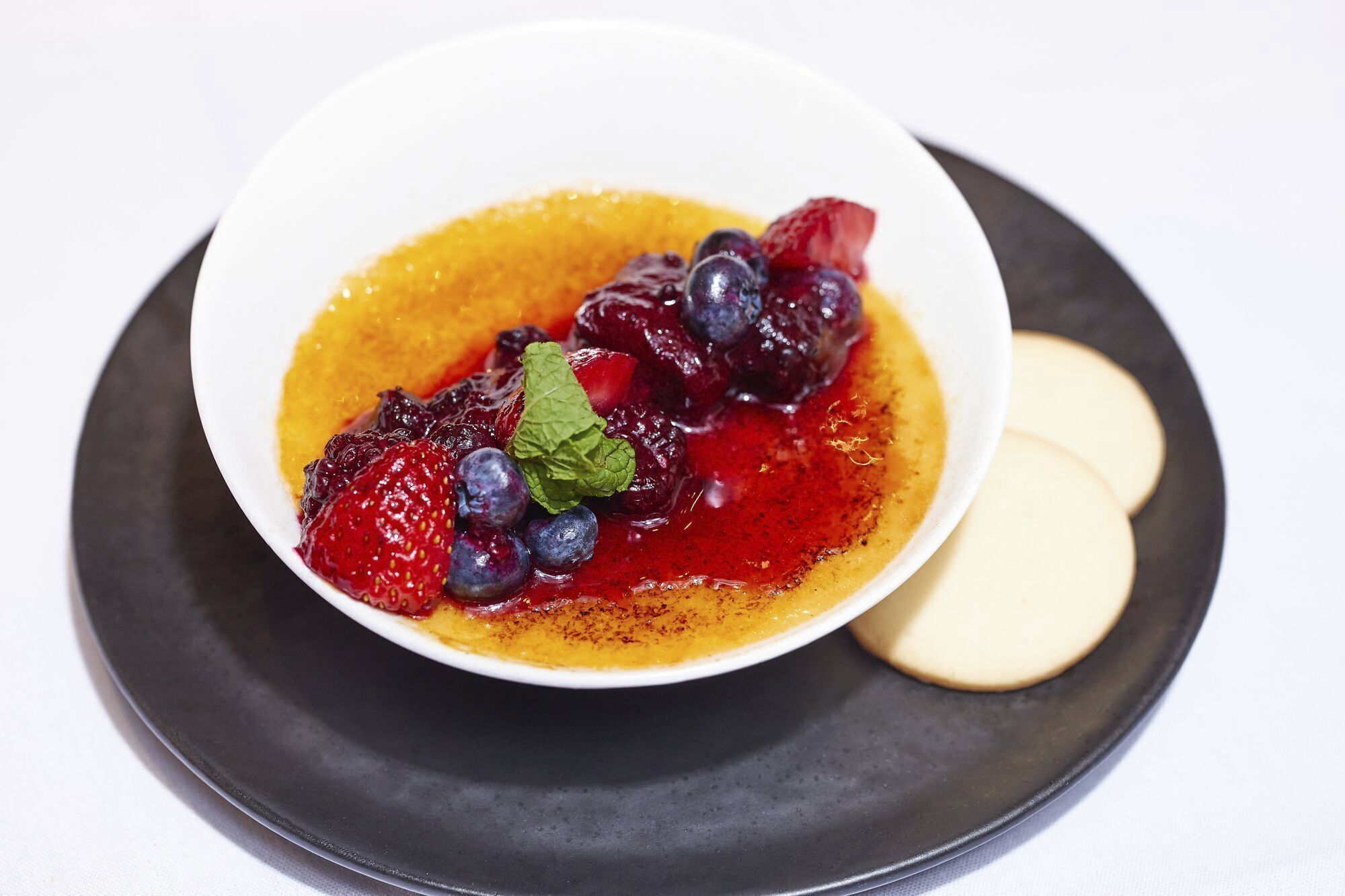 A dessert with berries and a mint leaf on a plate.