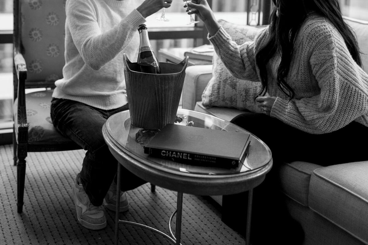 Two people sitting at a table with a bottle of champagne and a book titled "CHANEL".