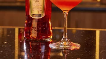 Una botella de Aperol y un vaso de cóctel con una rodaja de naranja como adorno sobre una superficie reflectante.
