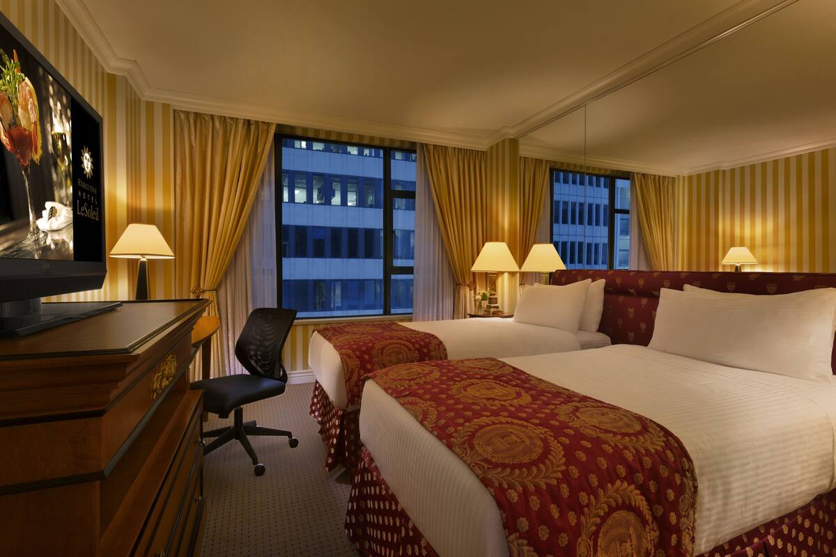 A hotel room with two beds, a desk, a chair, and a television.