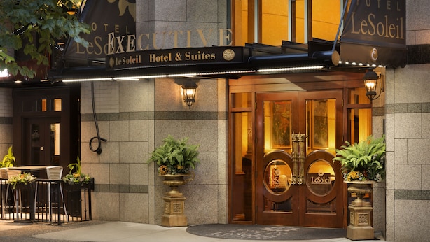 The exterior of Hotel Le Soleil, featuring a grand entrance with double doors, a signboard above, and outdoor seating with potted plants.