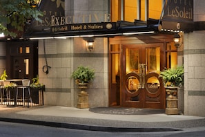 Exterior del Hotel Le Soleil, con una entrada imponente con puertas dobles, un cartel arriba y mobiliario exterior con plantas en macetas.