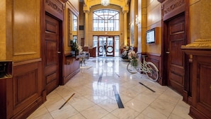 A grand lobby with marble floors, large wooden doors, and a chandelier.