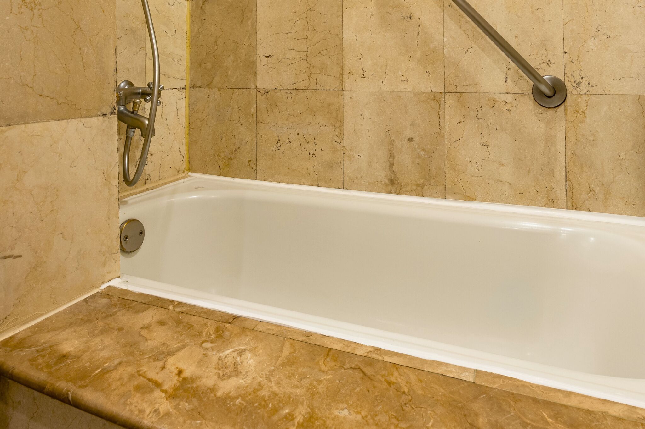 Une baignoire équipée d’un pommeau de douche, d’une barre d’appui et d’un mur recouvert de carreaux de marbre.