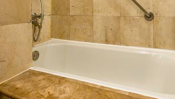 A bathtub with a showerhead, a grab bar, and a marble-tiled wall.
