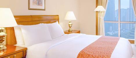 A hotel room with a large bed, two bedside tables with lamps, a framed picture on the wall, and a view of buildings through the window.