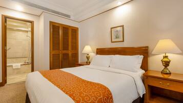 Habitación de hotel con una cama grande, dos lámparas de noche, una mesita de noche de madera, un armario de madera y una zona de ducha.