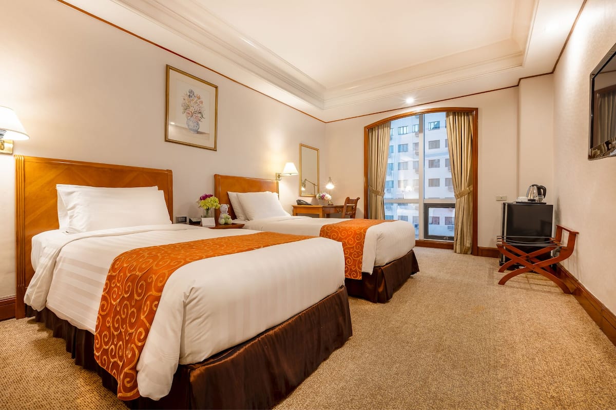 A hotel room with two beds, a TV, a desk with a lamp, and a window with curtains.