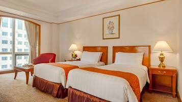 Une chambre d’hôtel avec deux lits, une chaise rouge, une petite table avec une lampe et une fenêtre avec des rideaux.