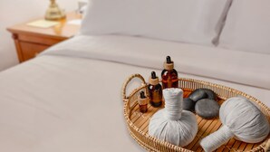 A neatly made bed with a white comforter and pillows, a bedside table with a lamp, and a tray with massage stones, oils, and a rolled-up towel. - Richmonde Hotel Ortigas (Pasig)