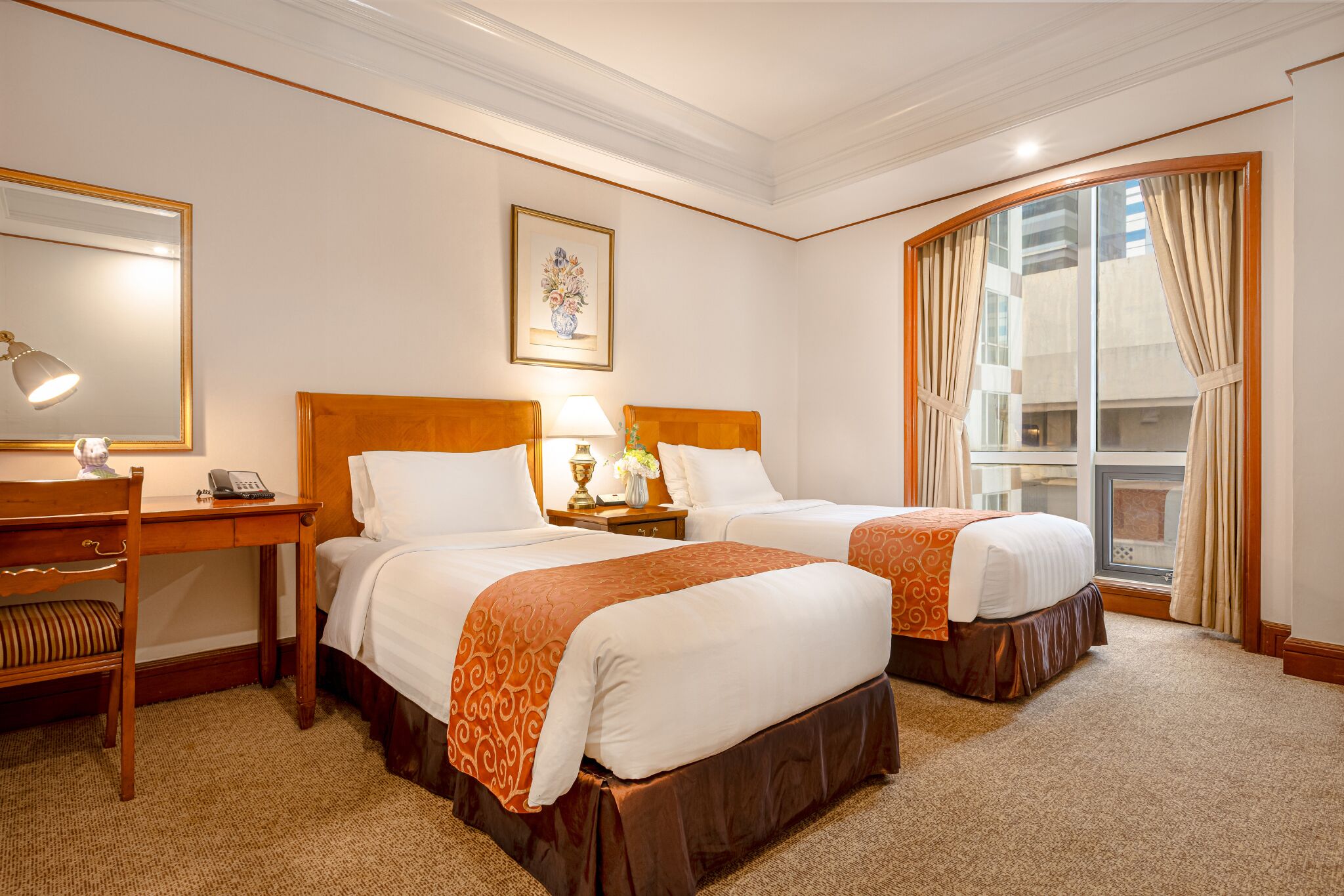 A hotel room with two beds, a desk, a chair, a telephone, a lamp, and a window with curtains.