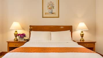 A hotel room with a wooden bed, two bedside tables with lamps, a framed floral artwork on the wall, and a vase with flowers on one of the tables.