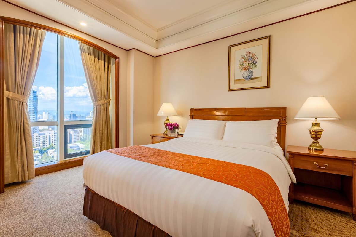 A hotel room with a large bed, two bedside tables with lamps, a window with curtains, and a framed picture on the wall.