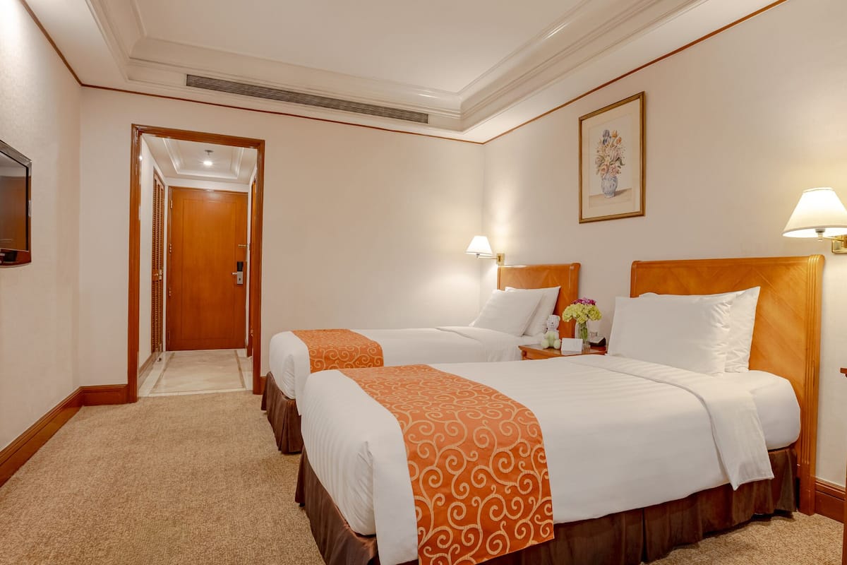 A hotel room with two beds, a television, and a hallway leading to another room.
