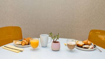 Una mesa de desayuno con croissants, zumo de naranja, café y una pequeña planta en maceta.