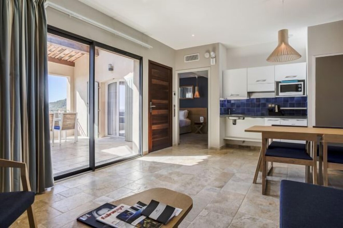 A modern kitchen with a microwave, stove, and blue tiled backsplash. There is a wooden dining table with blue chairs and a magazine on it.