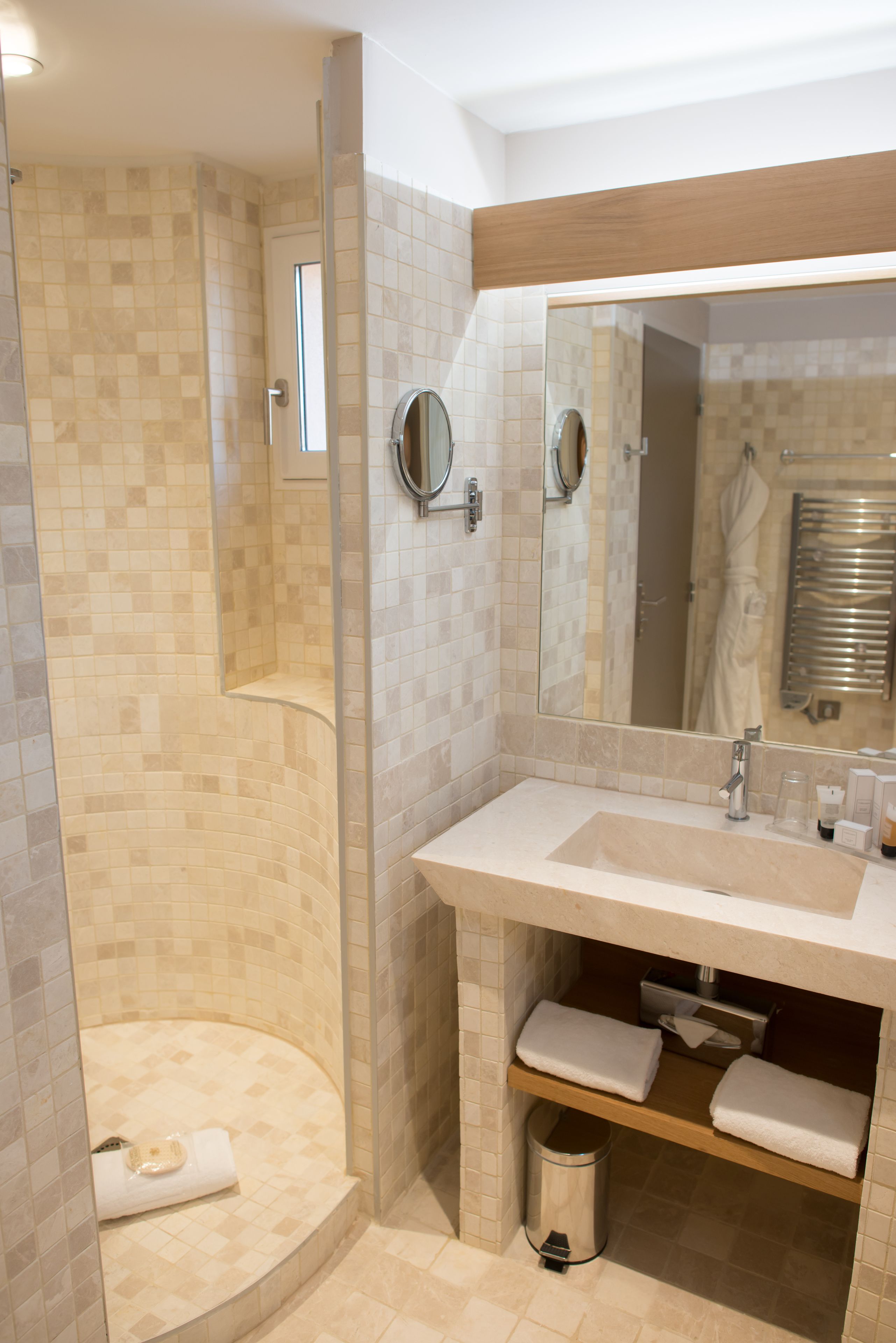 A bathroom with a shower, sink, mirror, and towel storage.