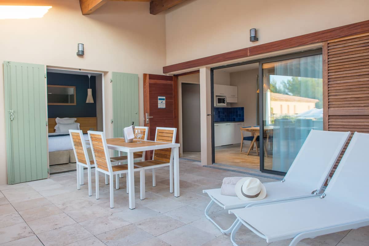 A room with a dining table and chairs, a lounge chair, and a sliding glass door leading to a kitchen area.