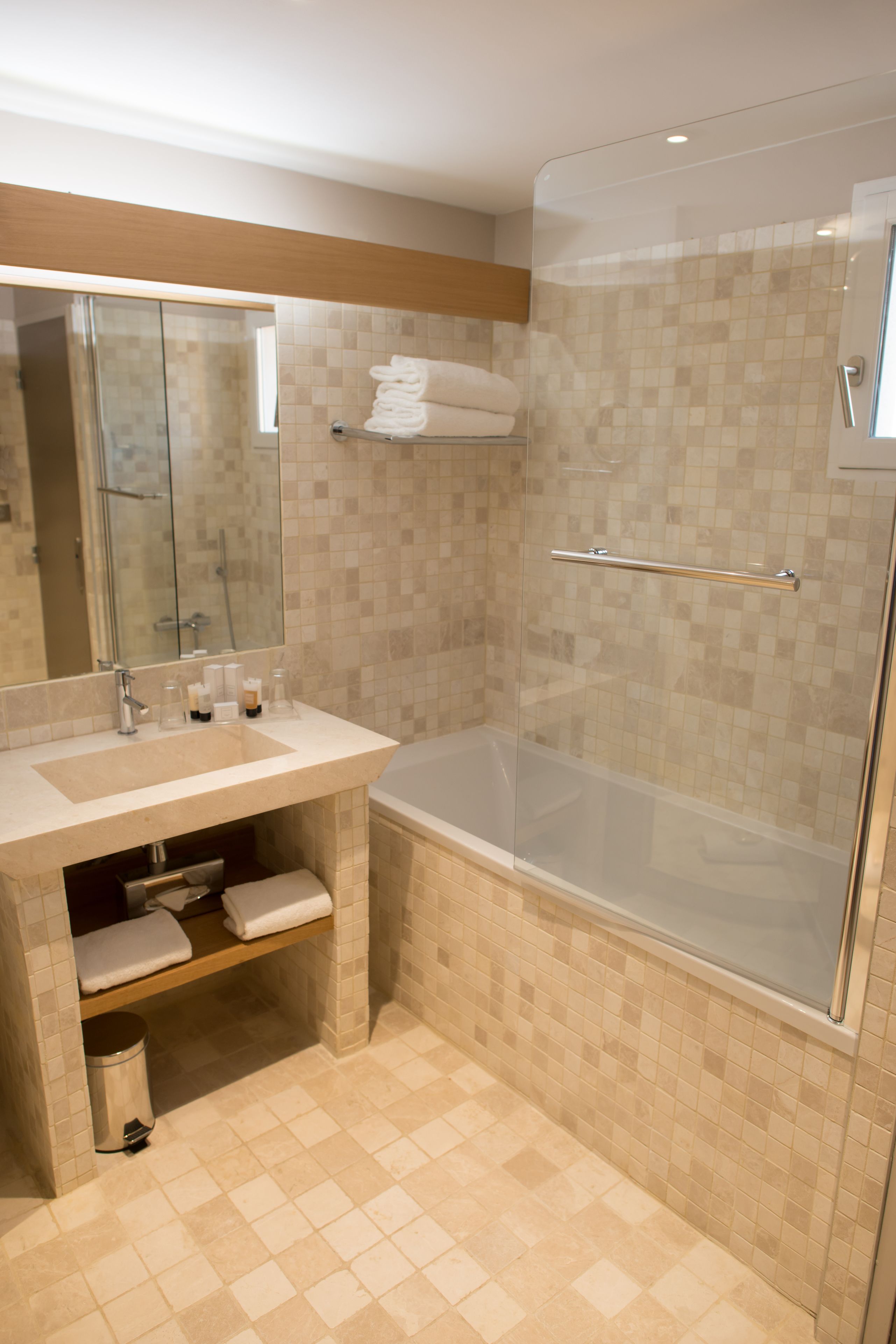 Un baño moderno con ducha envuelta en vidrio, tocador con espejo y suelo de baldosas.