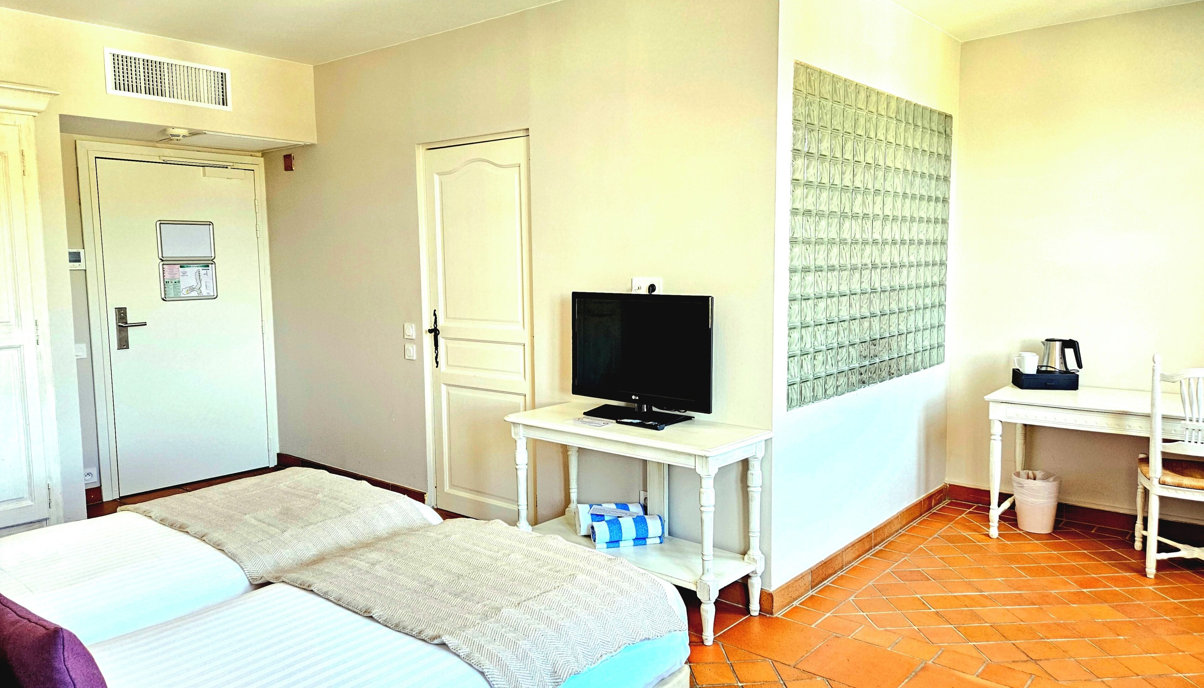 Quarto de hotel com uma cama, televisão sobre uma mesinha, escrivaninha com cadeira e um cesto de lixo.