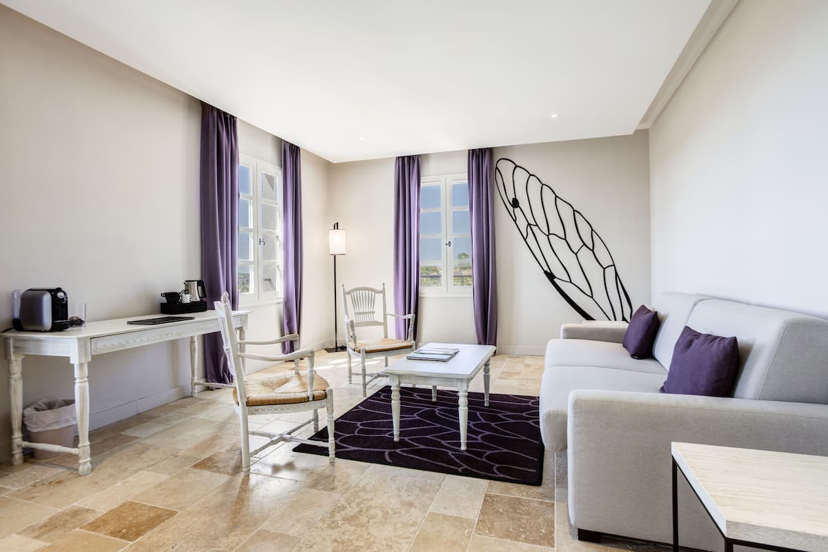 A modern living room with a sofa, a dining table, chairs, a coffee machine, and a large window with purple curtains.