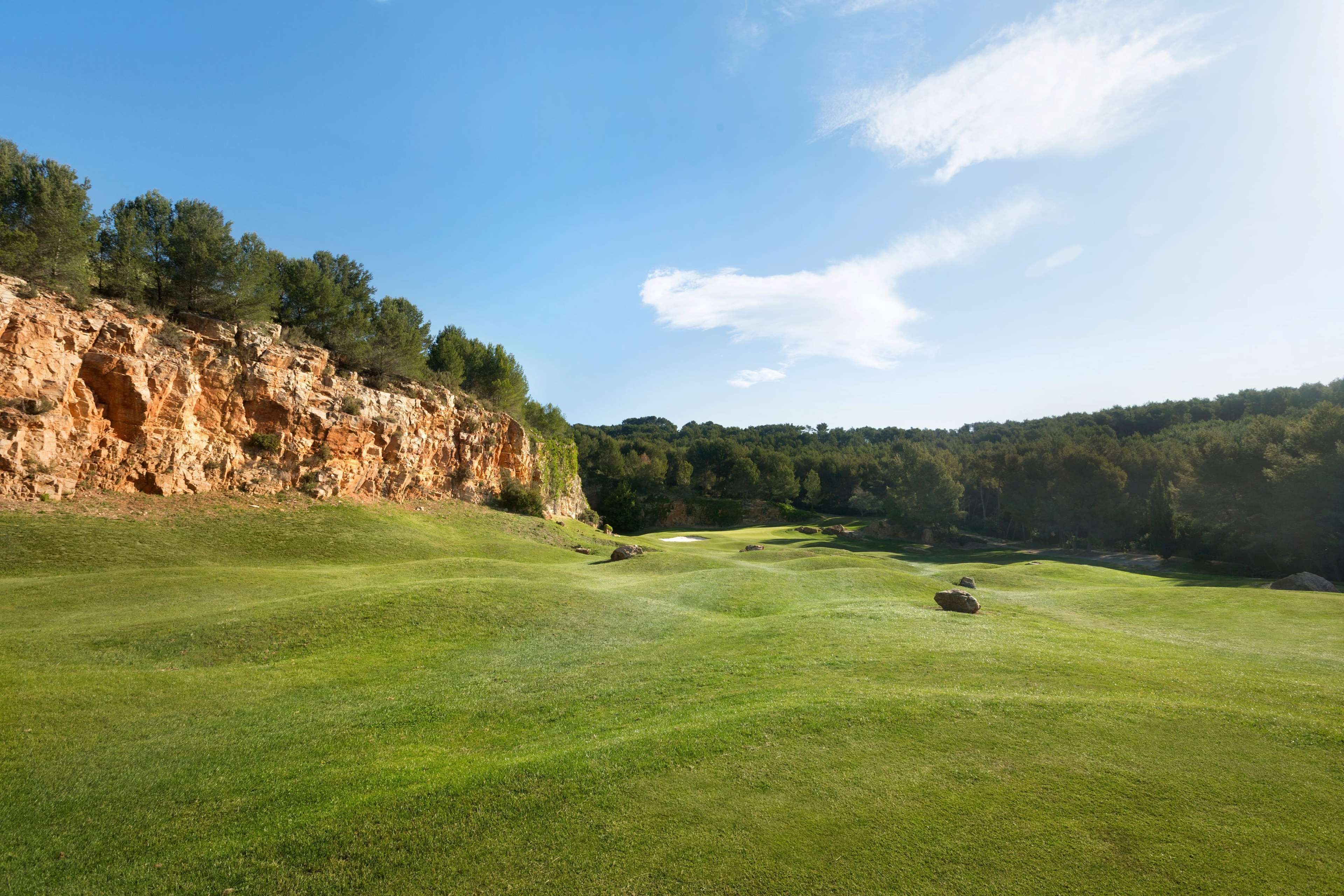 Un campo de golf con un acantilado rocoso y un denso bosque al fondo.
