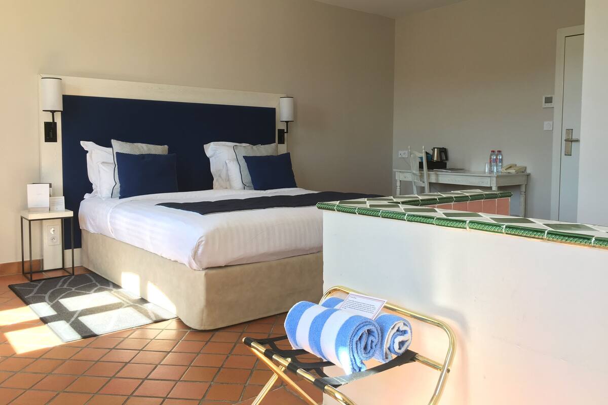 A hotel room with a bed, bedside table, lamp, and a desk with a chair.