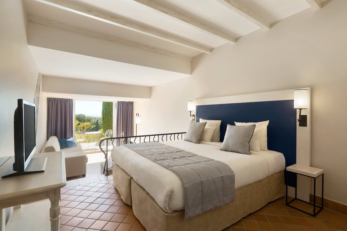 A bedroom with a bed, bedside table, TV, and a balcony with a view.