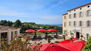 A terrace with red umbrellas, outdoor seating, and a view of the sea. - Le Frégate Provence (Saint-Cyr-sur-Mer)