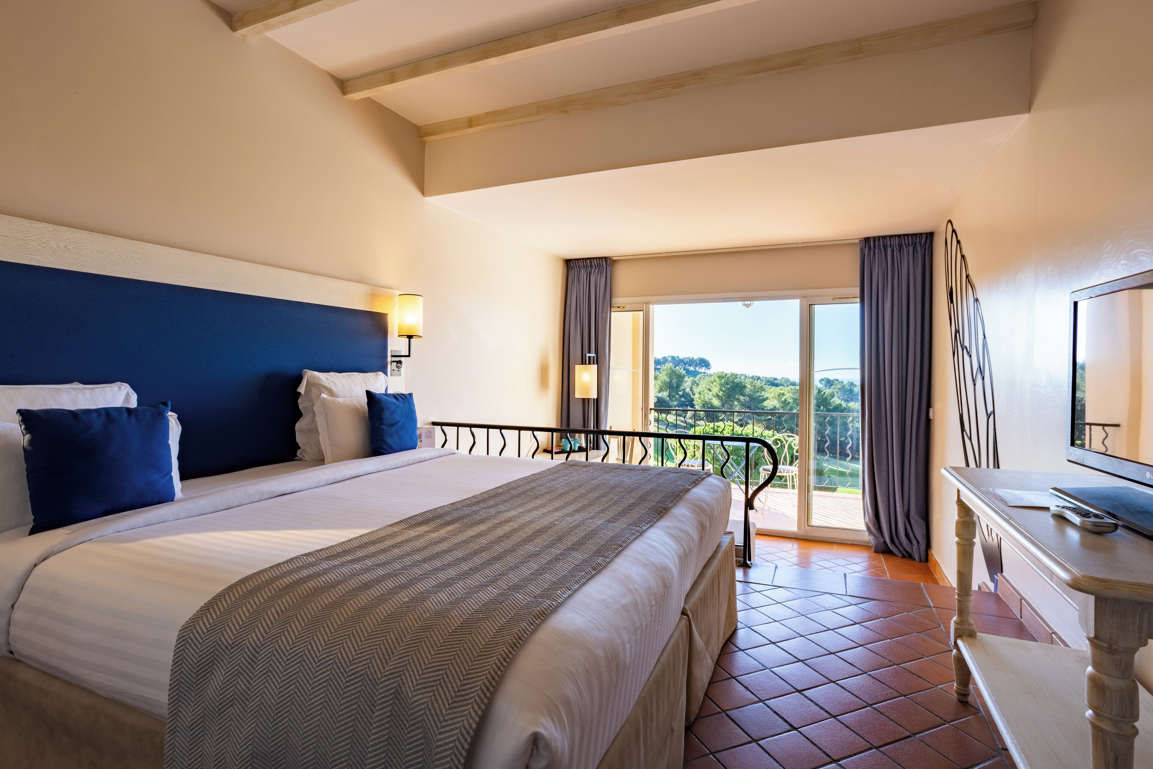 Habitación de hotel con una cama grande, televisión, balcón con vistas al campo y zona de comedor.