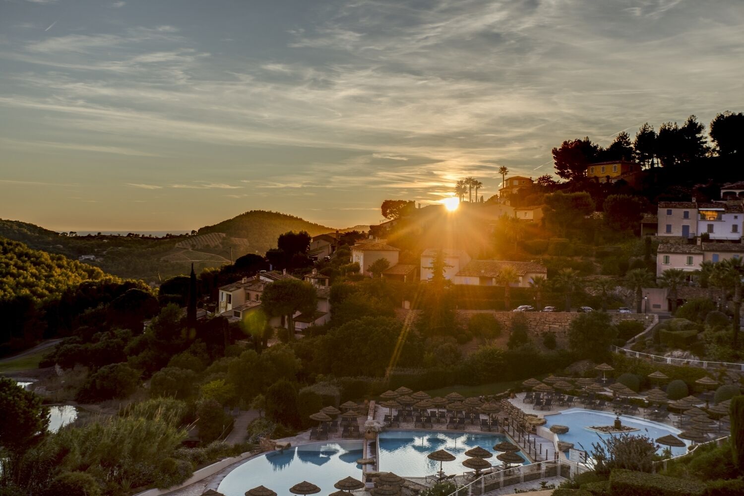 Un resort con piscina, sombrillas de techo de paja y vistas al atardecer.