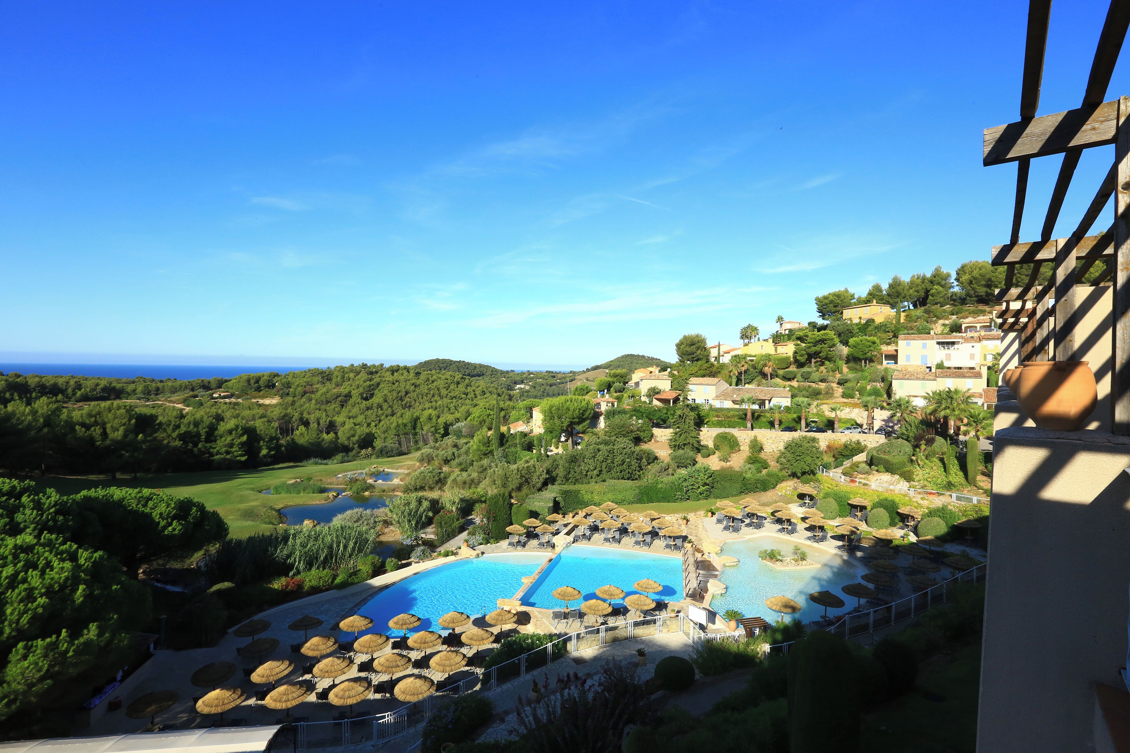 A resort with a large swimming pool, sun loungers, and a view of the surrounding greenery and hills.