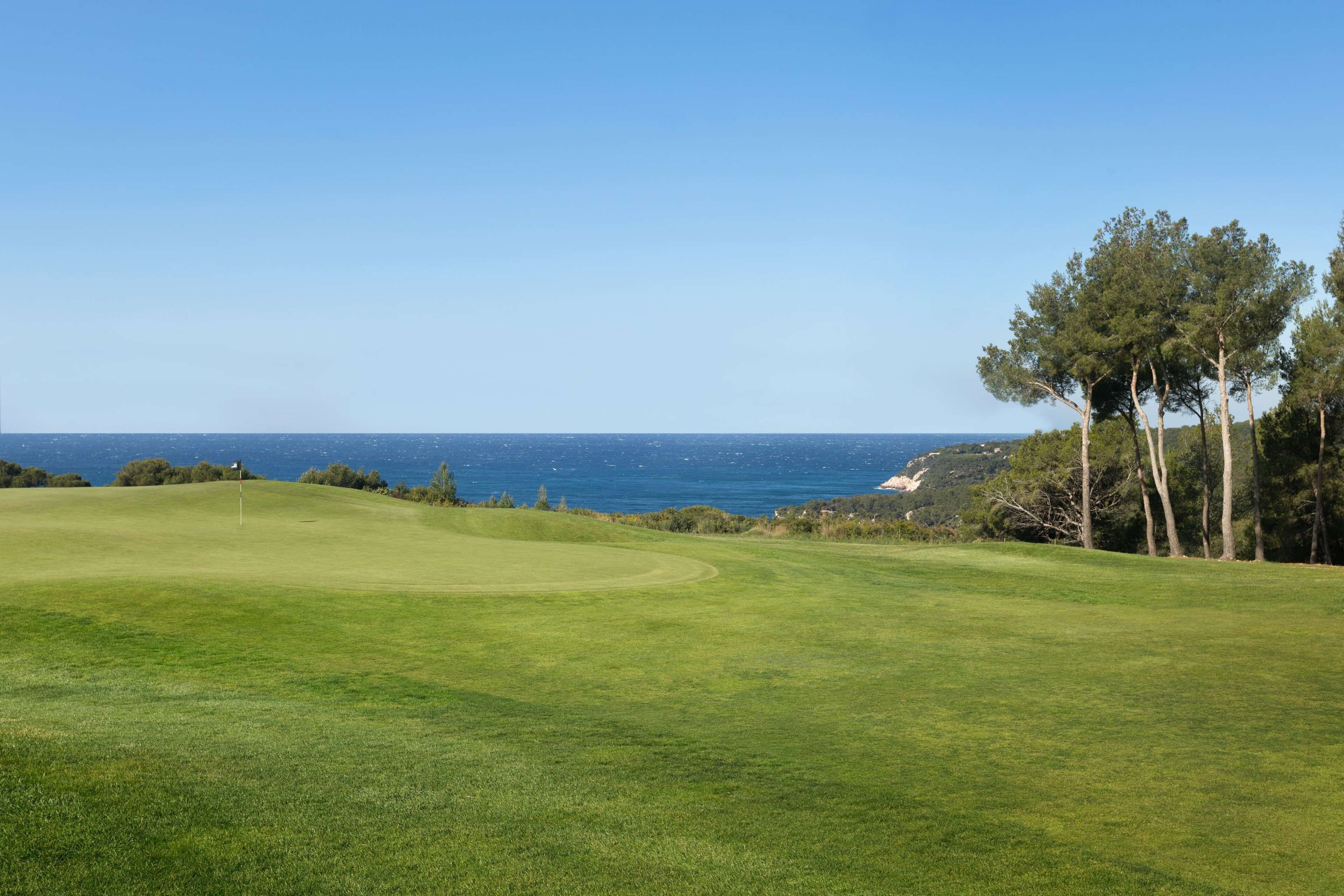 A golf course with a clear view of the ocean and a flagstick in the center.