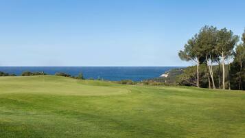 Un campo de golf con vista despejada al océano e un mástil con bandera en el centro.