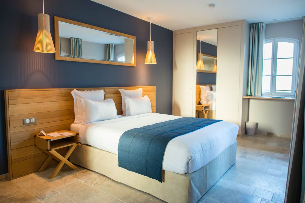A neatly made bed with a blue blanket, wooden headboard, and bedside table with a lamp.