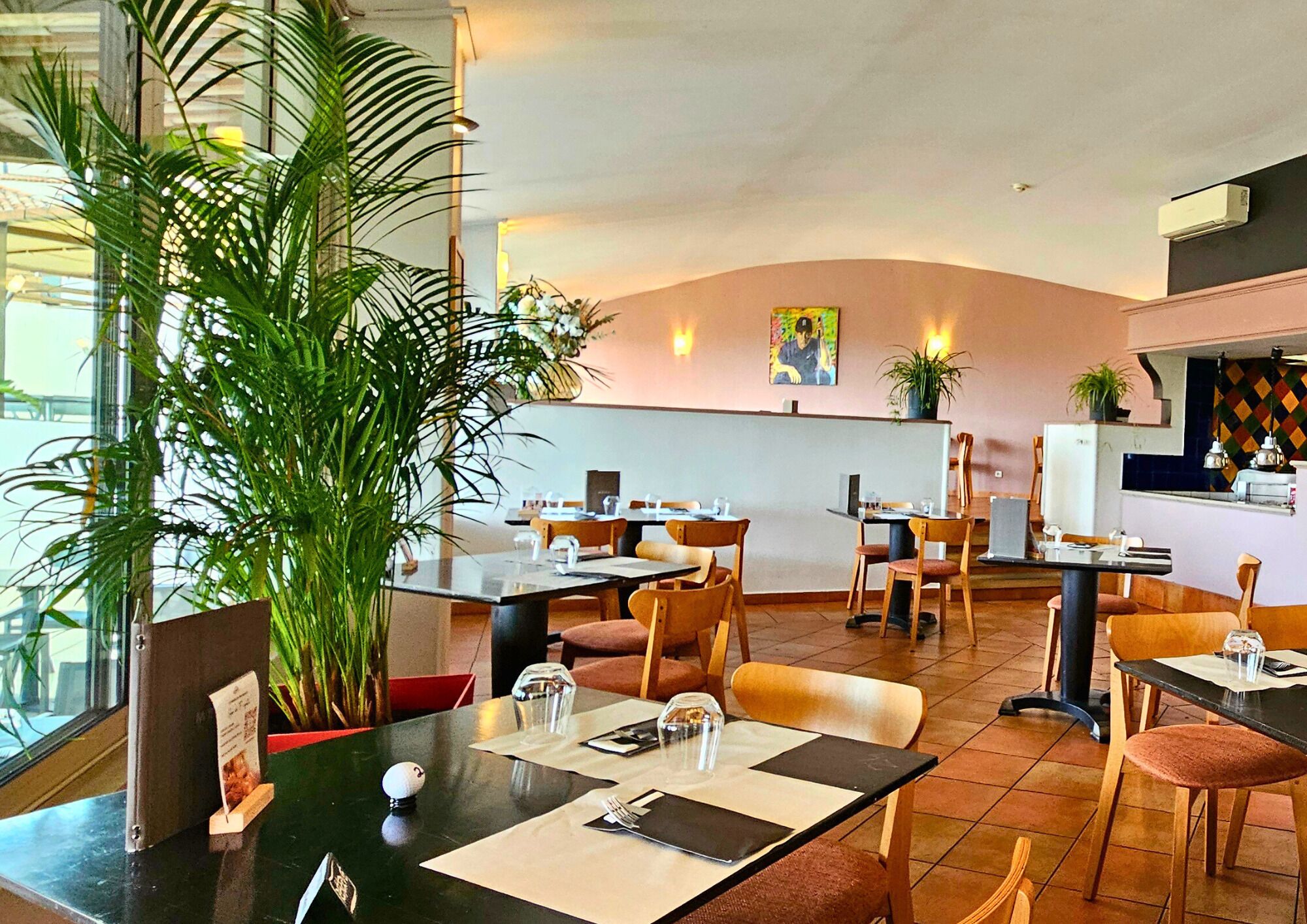 Un restaurante con mesas dispuestas para comer, sillas y una planta grande en maceta.