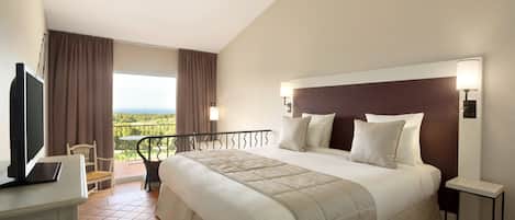 A hotel room with a large bed, a desk with a laptop, a TV, and a balcony with a view.