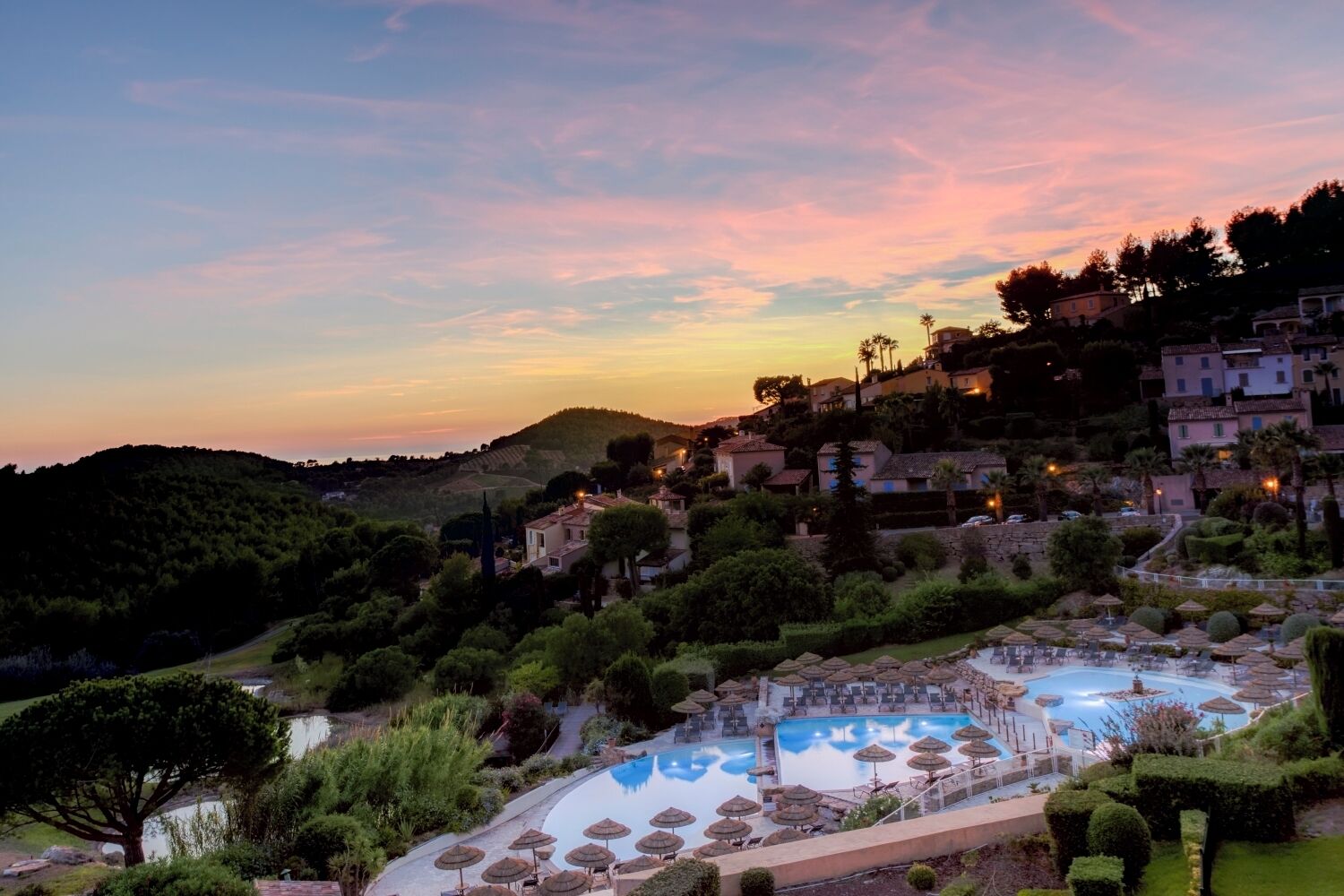 Un resort con piscina, rodeado de exuberante vegetación y colinas.