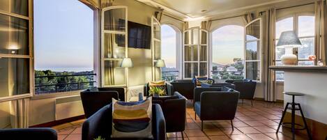 A spacious balcony with comfortable seating, large windows offering a city view, and a small bar area.