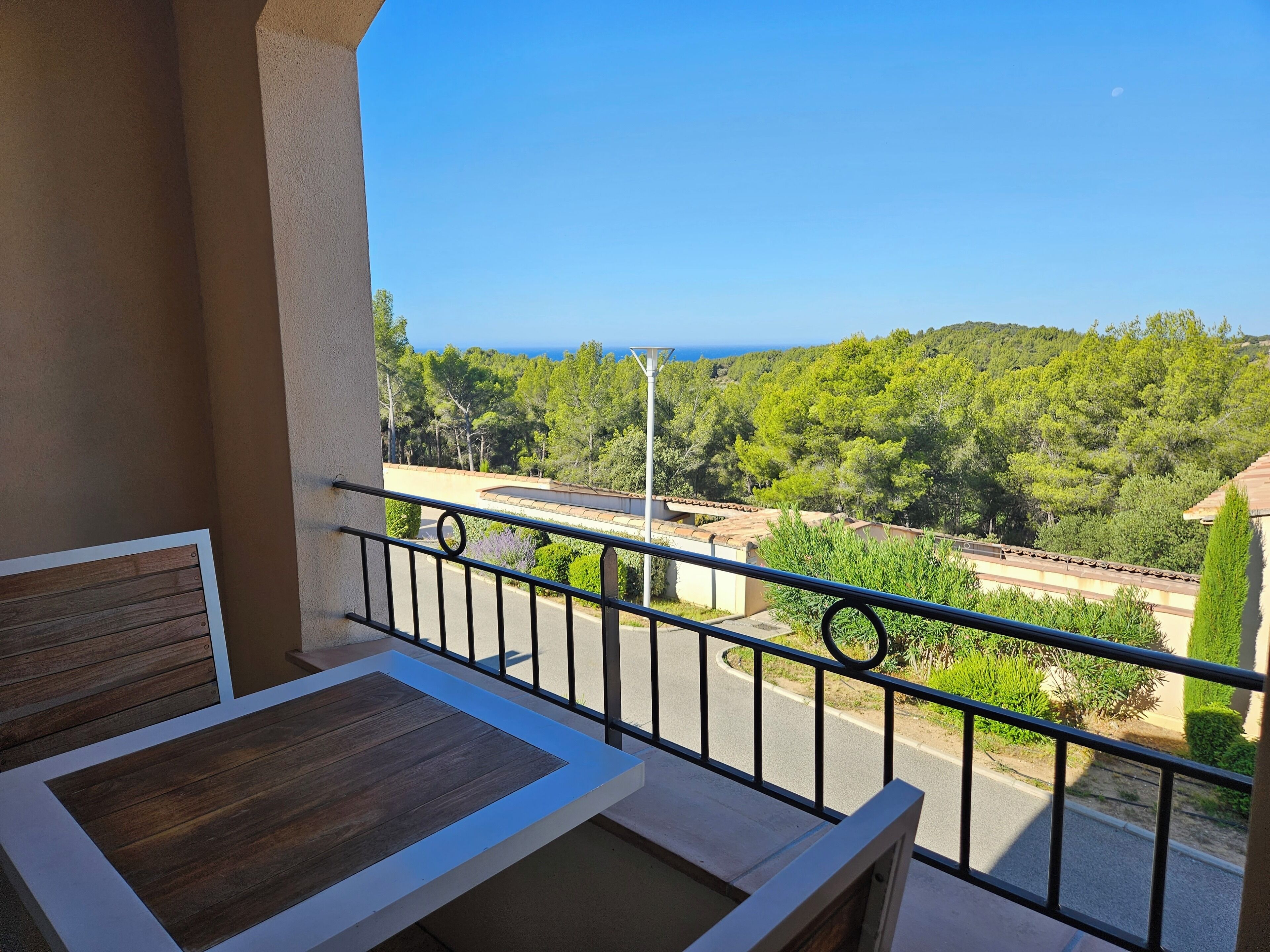 A balcony with a wooden table and a view of a road and greenery.
