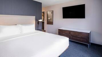 A hotel room with a large bed, a flat-screen TV mounted on the wall, a dresser, and a bedside lamp.
