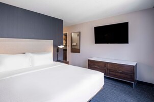 A hotel room with a large bed, a flat-screen TV mounted on the wall, a dresser, and a bedside lamp.