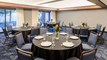 A conference room with round tables, chairs, and a large window with curtains.