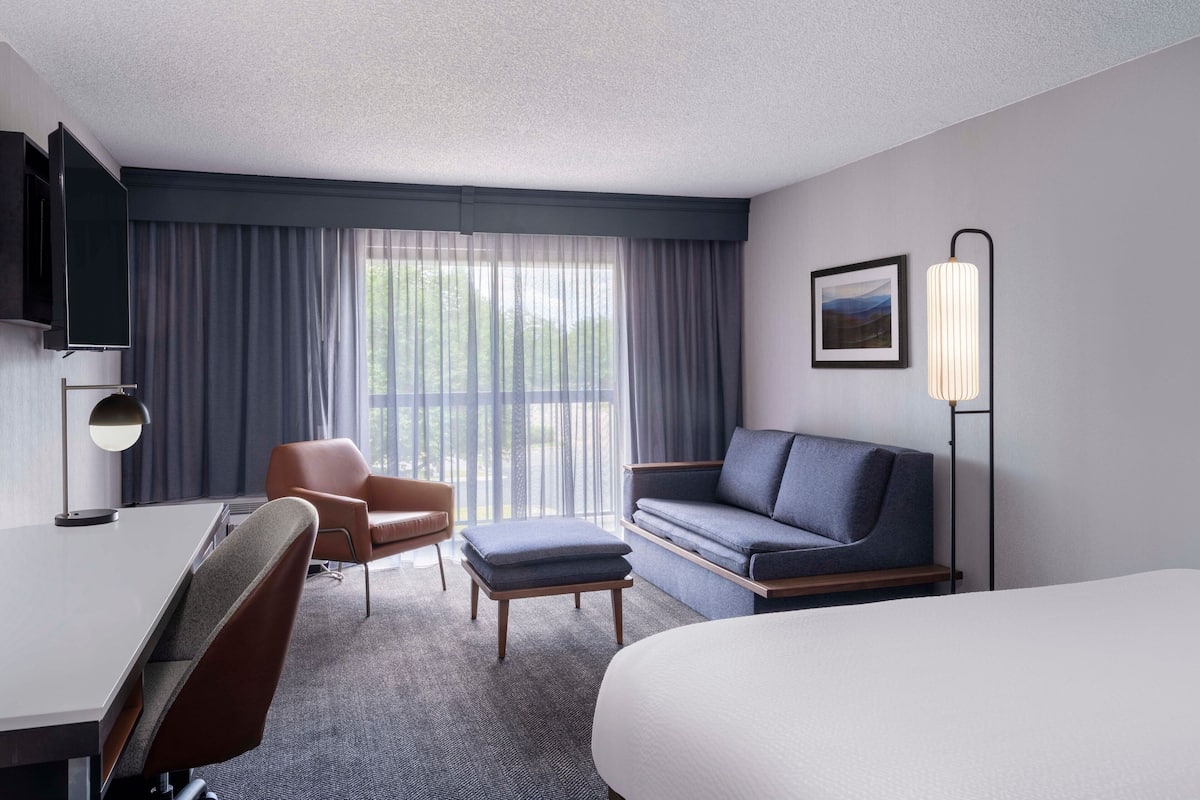 Ein Hotelzimmer mit Bett, Schreibtisch, Sessel, Sofa und Fernseher.