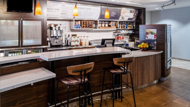 Un espace bar moderne avec un comptoir en bois, des tabourets de bar et un tableau affichant le menu.