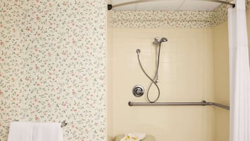 Een badkamer met bloemenbehang, een douche met een handgreep en een handdoekhouder.