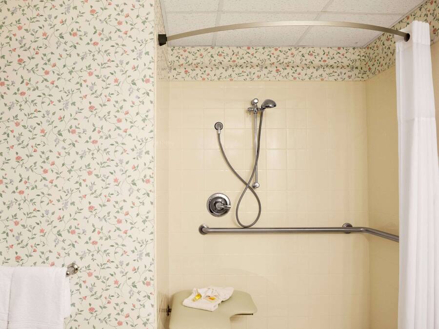 Un baño con papel tapiz floral, una ducha con barra de apoyo y un perchero para toallas.