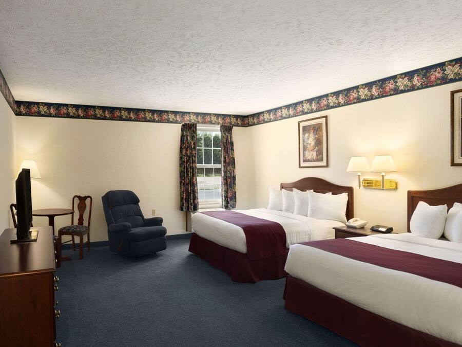 A hotel room with two beds, a desk, a chair, a television, and a window with curtains.