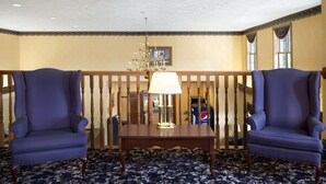 Ein Zimmer mit zwei blauen Sesseln, einem Holztisch mit Lampe, einer Chandelierleuchtre und einem gemusterten Teppich.